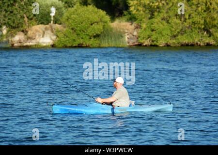 Un vero pescatore felice con catturato piccoli bassi sul suo colore blu kayak sul lago chiara Clearlake California USA America sulla tranquilla giornata di sole in estate da se stesso Foto Stock