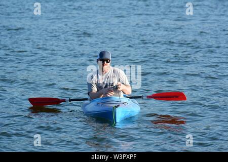 Un vero pescatore felice con catturato piccoli bassi sul suo colore blu kayak sul lago chiara Clearlake California USA America sulla tranquilla giornata di sole in estate da se stesso Foto Stock