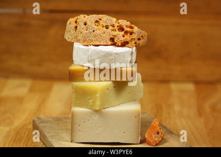 Pila di diversi tipi di formaggio sulla tavola di legno - formaggio di capra, mimolette e camembert Foto Stock