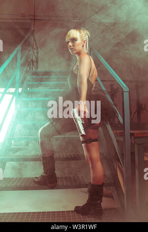 Ragazza bionda con pistole in una fabbrica abbandonata. cosplayer, azione e pericolosa donna Foto Stock