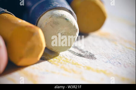 Pastello olio in pastelli di diversi colori - giallo ocra e bianco, avvolto in un involucro, giacente sulla carta per disegnare Foto Stock
