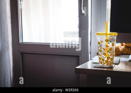 Un bicchiere con una cannuccia con dipinto di limoni sulla scrivania di un ufficio di casa vicino al computer. Foto Stock