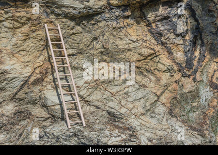 Piccolo giocattolo di legno scaletta sostennero contro la scogliera. Metafora la scalata di carriera, salire sull'alloggiamento scaletta, scala aziendale, arrampicata sociale. Foto Stock