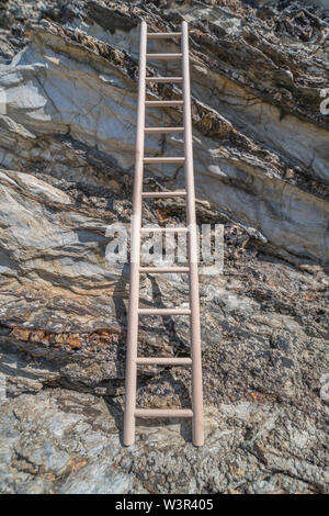 Piccolo giocattolo di legno scaletta sostennero contro la scogliera. Metafora la scalata di carriera, salire sull'alloggiamento scaletta, scala aziendale, arrampicata sociale. Foto Stock