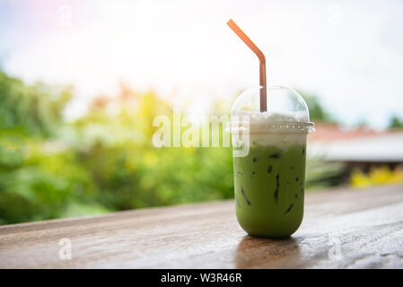 Iced tè verde in una tazza di plastica / tè verde Matcha latte frappé e paglia sul tavolo di legno con lo sfondo della natura Foto Stock