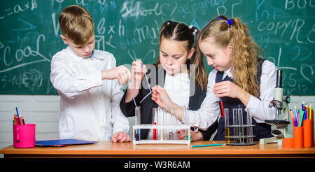 Concetto di lavoro di squadra. Provette con colorati di sostanze liquide. Studio di stati di liquido. Scuola di gruppo gli allievi studiano prodotti chimici liquidi. Laboratorio scolastico. Le ragazze e i ragazzi condotta esperimento con liquidi. Foto Stock