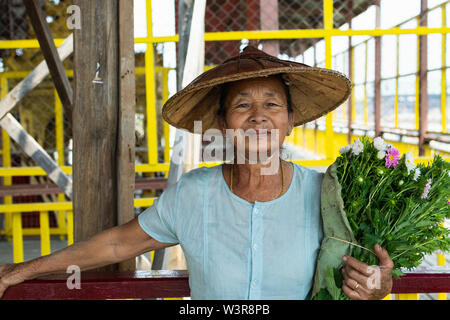Maing Thauk, Myanmar - Aprile 2019: ritratto di un vecchio birmano donna sorridente in un cappello di bambù e fiori. Foto Stock