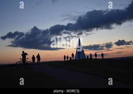 Alba del solstizio d'estate presso la Piramide di Luce in Campbell Park, Milton Keynes. Una dozzina di persone (non identificabili) sono a guardare il tramonto. Foto Stock