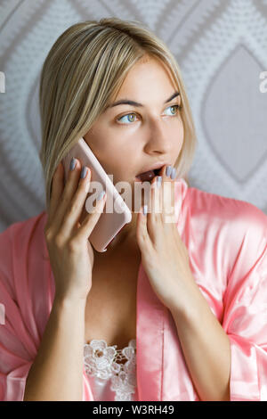 Giovane bella donna bionda vestito in abiti da casa emotivamente parlato al telefono di casa Foto Stock