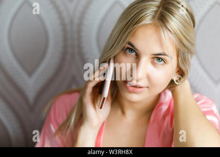 Giovane bella donna bionda vestito in abiti da casa emotivamente parlato al telefono di casa Foto Stock