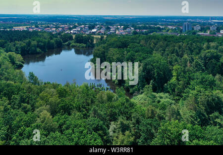 Vista aerea di un territorio densamente ricoperta di verde area di foresta con un grande vecchio stagno e le case della città in background. Foto Stock