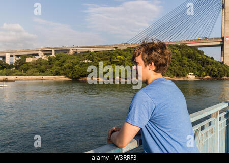 Un giovane ragazzo in piedi sul molo e guardando il mare Foto Stock