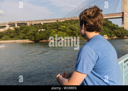 Un giovane ragazzo in piedi sul molo e guardando il mare Foto Stock