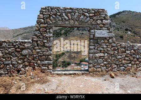 Muro di pietra e una vista attraverso un cancello abbandonati a Hydra Island, Grecia. Foto Stock