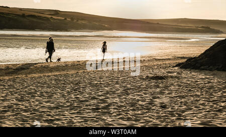Una famiglia di tre persone e un cane a camminare lungo la riva del mare con il sole di sera sull'estuario del cammello con la bassa marea in North Cornwall. Foto Stock
