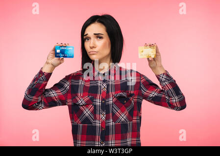 Giovane donna in rosso plaid shirt mostra due carte di credito su sfondo rosa Foto Stock