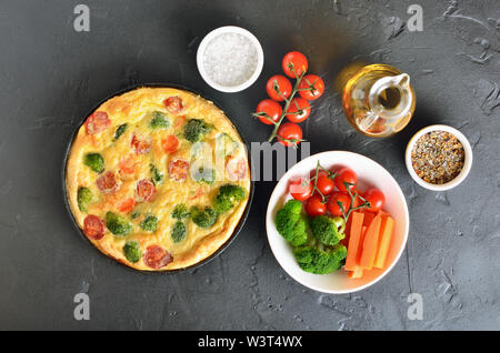 Frittata con broccoli e pomodori in padella su sfondo nero, vista dall'alto Foto Stock