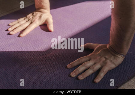 Close up man mano mentre facendo una postura yoga su un tappeto colorati. Lo Yoga, sano e il concetto di benessere Foto Stock