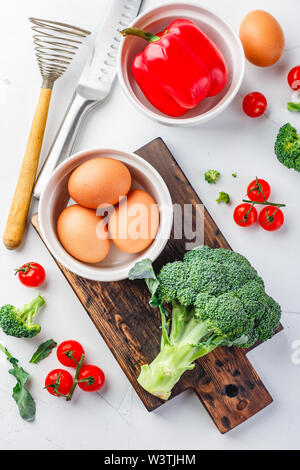 Ingredienti per la cottura di uova frittata e verdure fresche - broccoli, peperoni, pomodori ciliegia su uno sfondo luminoso. Vista da sopra Foto Stock