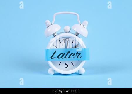 La procrastinazione, ritardo e concetto di urgenza. White orologio sveglia con una nota adesiva con il testo più tardi. Foto Stock