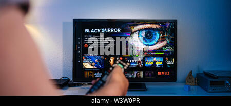 Parigi, Francia - Luglio 10, 2019: Senior man mano che tiene il telecomando a guardare il Black Mirror su Netflix - British science fiction televisione serie creata da Charlie Brooker selezionando episodio Foto Stock