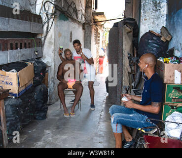 Un barbiere taglia i suoi clienti i capelli in un barbiere di fortuna in un vicolo a l'Avana, Cuba Foto Stock