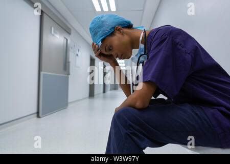 Chirurgo teso con la mano sulla fronte seduto nel corridoio di un ospedale Foto Stock