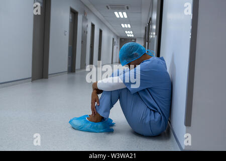 Teso chirurgo femmina seduta con gli occhi chiusi nel corridoio Foto Stock
