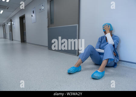 Teso chirurgo femmina seduta nel corridoio di ospedale Foto Stock