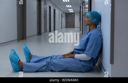 Teso chirurgo femmina seduta con gli occhi chiusi nel corridoio Foto Stock