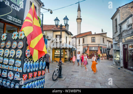 SKOPJE, Macedonia nord-Agosto 23 2019:Vecchio Bazar,bandiera macedone pende al di fuori tourist souvenir shop,con scene di strada e Moschea,sfocato nella backg Foto Stock