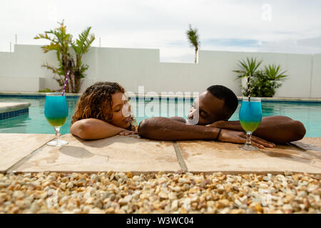 Coppia con bicchieri da cocktail appoggiata sul bordo di una piscina Foto Stock