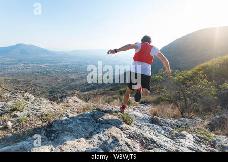 Una forte, atheletic l uomo è visto da dietro mentre corre giù full tilt su un arido, sentiero roccioso nelle montagne di El Arenal, hidalgo, Messico, come s Foto Stock
