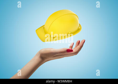 Femmina con mano gialla costruzione elmetto su sfondo blu Foto Stock