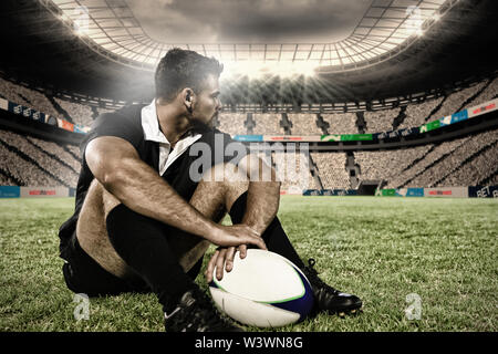 Immagine composita del rugby giocatore seduto sul campo con il calcio. Foto Stock
