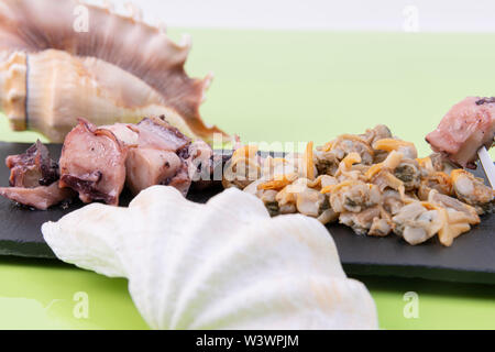 Close-up di gustosi piatti a base di frutti di mare, cardidi servita con potón su una piastra nera con conchiglie di mare decorare la foto su un verde foto Foto Stock