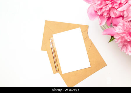 Vista superiore dello spazio di lavoro femminile invito a nozze card mockup con le peonie fiori su sfondo rosa. Lay piatto Foto Stock