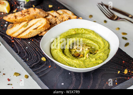 Hummus con spinaci e i semi di zucca in una ciotola su una tavola di legno, cucina orientale, la foto in orizzontale Foto Stock