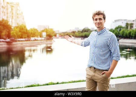 Giovane uomo casual elegante vestito guardando con fiducia alla telecamera presentando una città europea con un fiume dietro Foto Stock