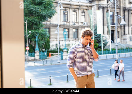 Giovane uomo a camminare e avere una conversazione al telefono cellulare all'ingresso di un vecchio edificio Foto Stock