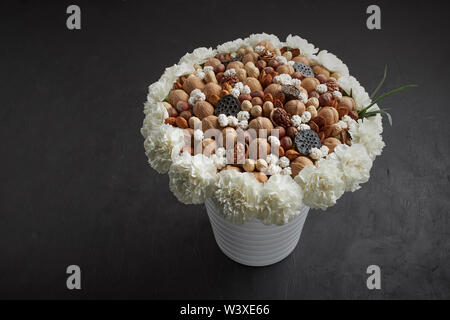 Bouquet unico costituito da diversi tipi di dadi, decorato con fiori di garofano bianco sorge in un vaso su sfondo nero Foto Stock