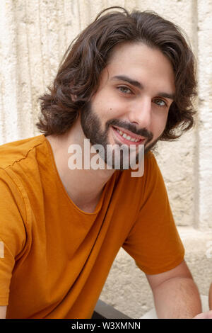 Ritratti di un giovane uomo sulla strada, guardando la fotocamera mentre il sorriso con una t-shirt arancione Foto Stock