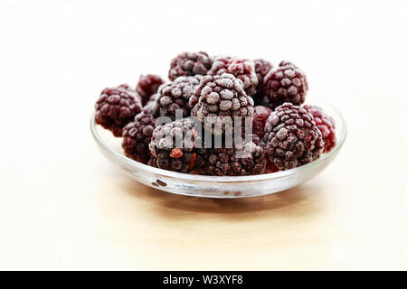 Piattino con il mucchio di congelati frutti blackberry su legno Foto Stock