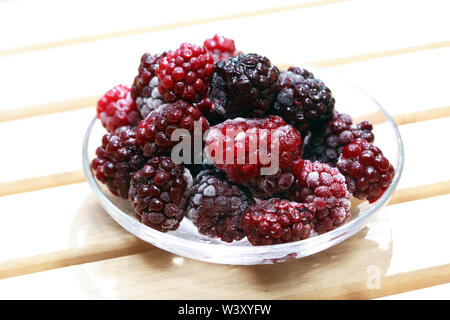 Piattino con il mucchio di congelati frutti blackberry su legno Foto Stock