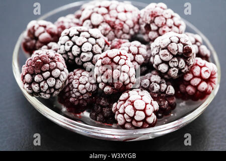 Piattino con il mucchio di congelati frutti neri su sfondo scuro Foto Stock