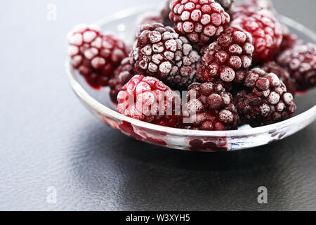 Piattino con il mucchio di congelati frutti neri su sfondo scuro Foto Stock