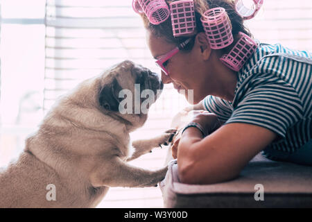 Amore e amicizia concetto con abbastanza caucasian giovane donna stabiliscono sul divano di casa e incantevole adorabile cane pug la bacia sul naso - curle Foto Stock