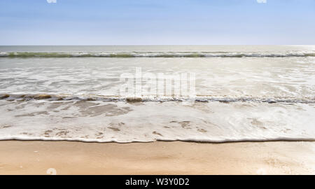 Che lambiscono dolcemente le onde su una spiaggia di sabbia con cielo blu Foto Stock