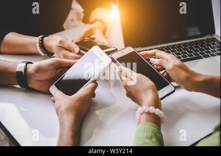 Gruppo di giovani hipsters tenendo il telefono in mano all'ufficio. Amici divertendosi insieme con gli smartphone. Tecnologia e concetto di comunicazione. Sc nero Foto Stock