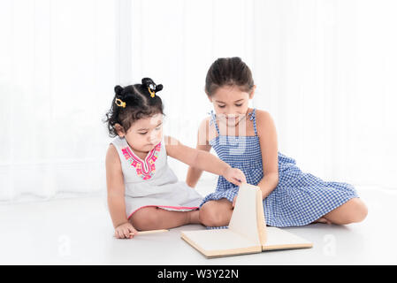 Felice due sorella disegno nel disegno libro insieme a casa o asilo nido. Lo stile di vita delle persone e bambini a giocare. L'istruzione e i bambini del concetto. Multiculturalità Foto Stock